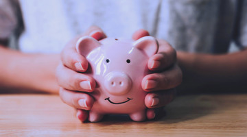 Deux mains tiennent une tirelire rose en forme de cochon avec un sourire.