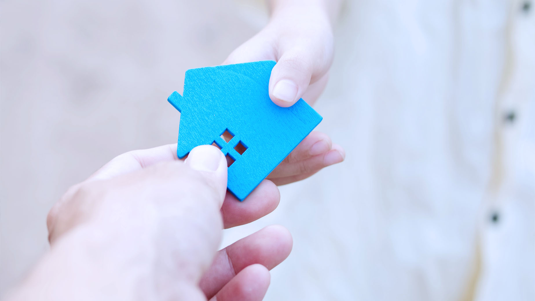 Une main tend un porte-clé en forme de maison bleue à une autre main.