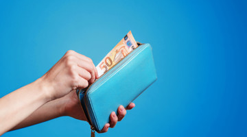 Hand haalt een €50 biljet uit een turquoise portemonnee tegen een blauwe achtergrond.