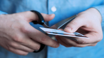 Een persoon knipt een plastic kaart doormidden met een schaar.