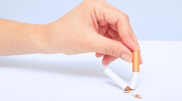 Une main casse une cigarette en deux, laissant tomber des résidus de tabac sur la table, symbolisant l'arrêt du tabac.