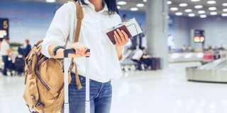 Vrouw met een handtas en handbagage die op de luchthaven haar boardingpas en paspoort controleert.