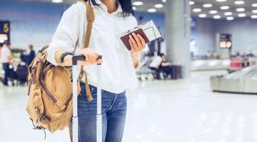 Vrouw met een handtas en handbagage die op de luchthaven haar boardingpas en paspoort controleert.