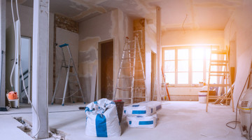 Lege ruimte voor renovatie met steigers, bouwmaterialen en veel natuurlijk licht afkomstig van een groot raam.