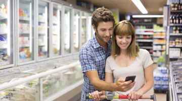 Un couple regarde un smartphone tandis qu'il se tient devant les vitrines réfrigérées d'un supermarché.