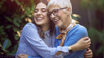 Deux personnes s'enlacent dans un milieu verdoyant, affichant des visages souriants et une langue corporelle chaleureuse et joyeuse.