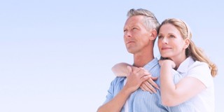 Un homme et une femme se tiennent ensemble, les bras l'un autour de l'autre, par une journée ensoleillée avec un ciel bleu clair en arrière-plan.