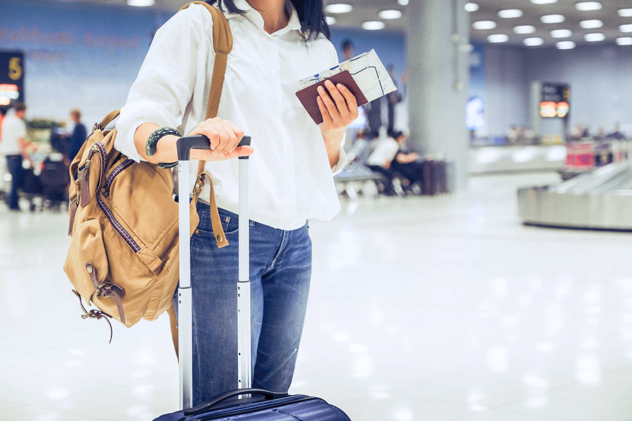 Femme avec un sac à dos et une valise, attendant ses bagages à l'aéroport avec des documents de voyage à la main.