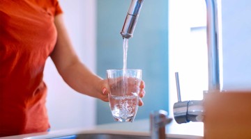 Une main tient un verre sous un robinet qui coule, alors que de l'eau claire est versée dans le verre.