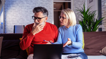 Un homme et une femme discutent de quelque chose alors qu'ils sont assis ensemble sur un banc, avec un ordinateur portable ouvert devant eux.