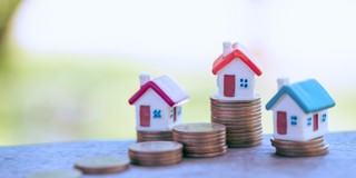 Trois maisons miniatures sur des piles de pièces, symbolisant la valeur immobilière et la croissance financière.