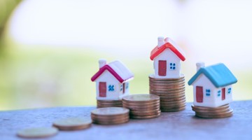 Trois maisons miniatures sur des piles de pièces, symbolisant la valeur immobilière et la croissance financière.