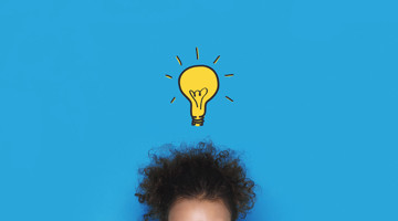 Une femme aux cheveux bouclés regarde vers le haut, vers une sphère lumineuse au-dessus de sa tête, symbolisant une idée ou une inspiration.