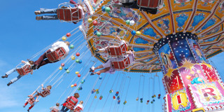 Des gens profitent d'un manège avec des sièges colorés suspendus dans les airs, sur fond d'un ciel bleu éclatant.