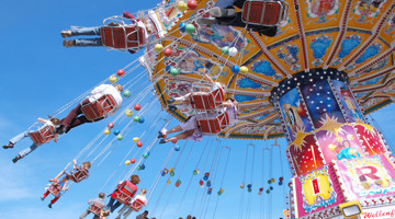 Des gens profitent d'un manège avec des sièges colorés suspendus dans les airs, sur fond d'un ciel bleu éclatant.