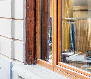 Hoek van een houten raam met een grote moderne glazen ruit in een lichte gevel.