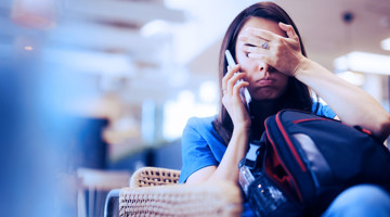 Femme en tenue bleue au téléphone, assise dans un espace moderne avec un sac à dos à côté d'elle.