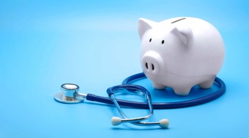 Witte spaarpot in de vorm van een varkentje naast een medische stethoscoop op een blauwe achtergrond, symboliseert financiële en gezondheidszorgplanning.