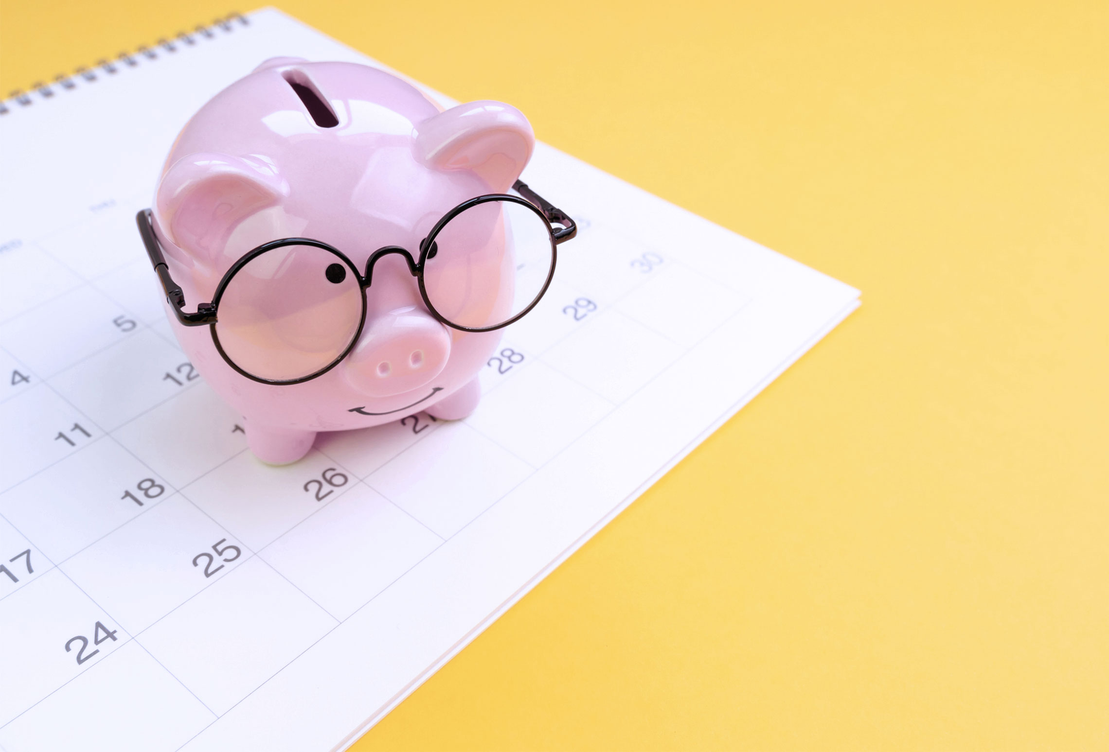 Roze spaarvarken met een bril op een kalender, benadrukt financiële planning en sparen.