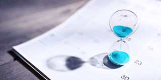Zandloper met turquoise zand op een kalender, symboliseert tijdbeheer en deadlines.