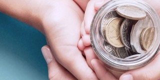 Deux mains tiennent un pot en verre rempli de pièces de monnaie, suggérant qu'il y a des économies précieuses en cours de collecte.