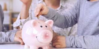 Des enfants mettent des pièces de monnaie dans une tirelire rose en forme de cochon, symbolisant l'épargne et l'éducation financière.