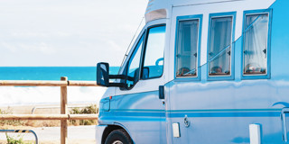 Camper parkeren aan het strand met op de achtergrond een blauwe zee en golven.