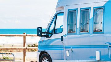 Camper parkeren aan het strand met op de achtergrond een blauwe zee en golven.