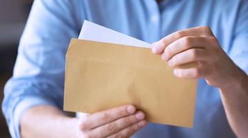 Une personne portant une blouse bleue tient une enveloppe brune et regarde à l'intérieur.