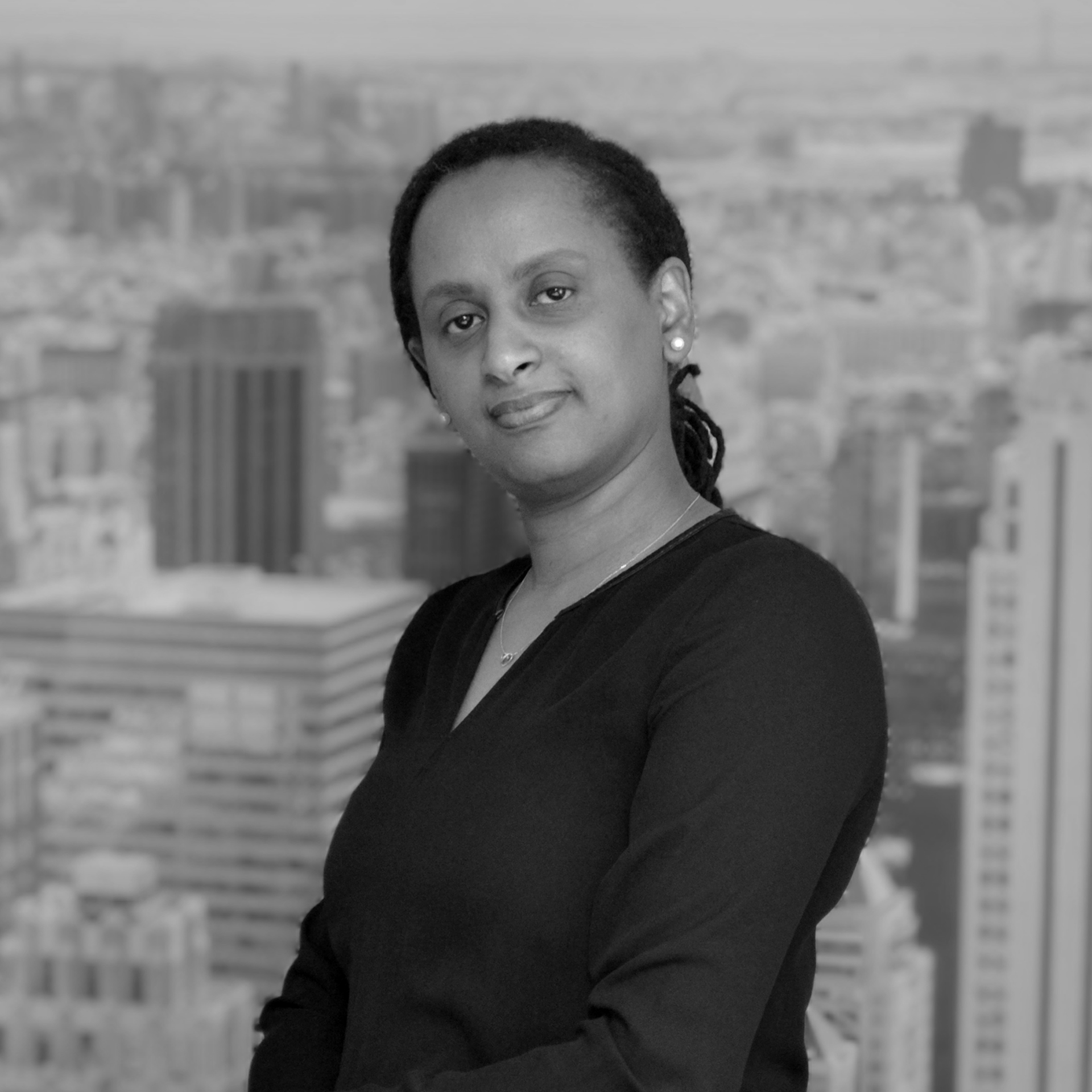 Vrouwelijke professional in zwart shirt, staande voor een zwart-witte stedelijke skyline.