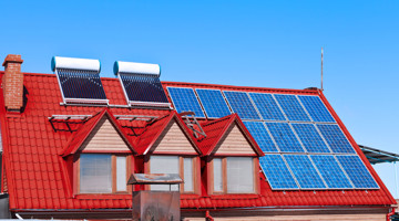 Rood dak met zonnepanelen en zonneboilers onder een heldere blauwe lucht.