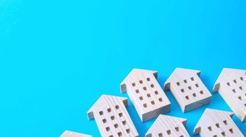 Houten huisjes in een rij op een blauwe achtergrond, symbool voor vastgoed of de woningmarkt.
