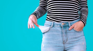 Femme en pull rayé montrant une poche de pantalon vide sur fond turquoise, symbolisant des difficultés financières.