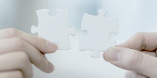 Deux petites mains tiennent différents morceaux de puzzle, prêtes à s'emboîter.