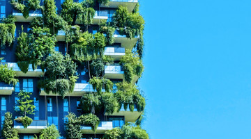 Façade verte d'un immeuble d'appartements moderne avec de nombreuses plantes et arbres sur les balcons, sur fond d'un ciel bleu clair.