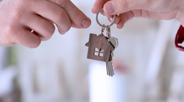 Une main remet une clé accompagnée d'un porte-clé en bois, symbolisant le transfert d'une maison.